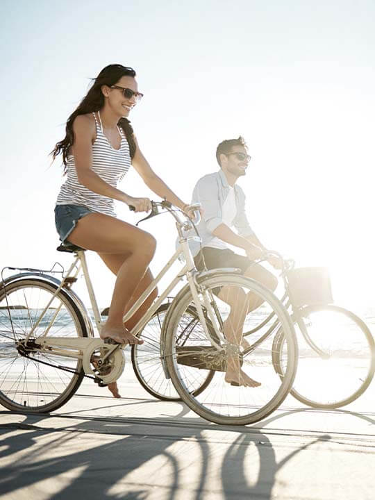 Bright Picture of Man and Women Riding Their Bikes Next to Ocean on The Sand